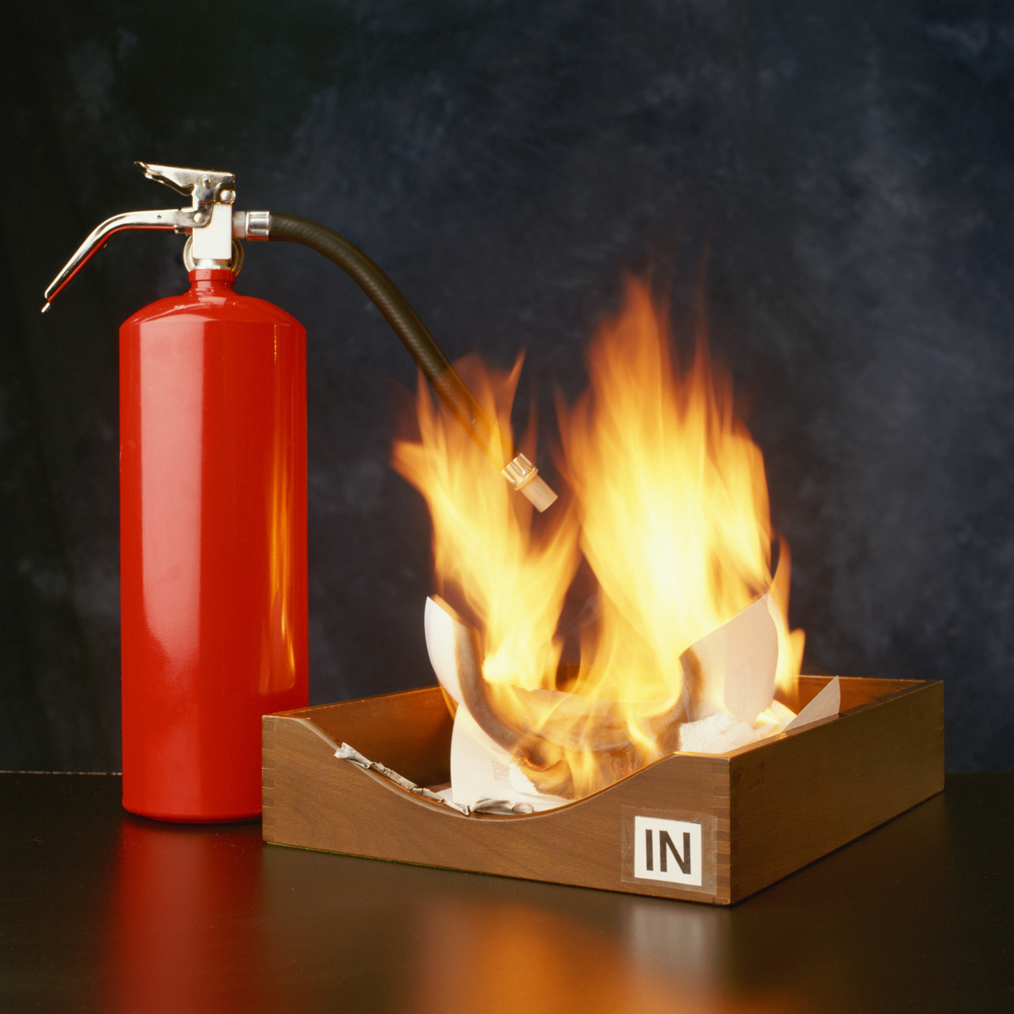 Fire extinguisher beside office tray containing burning paper